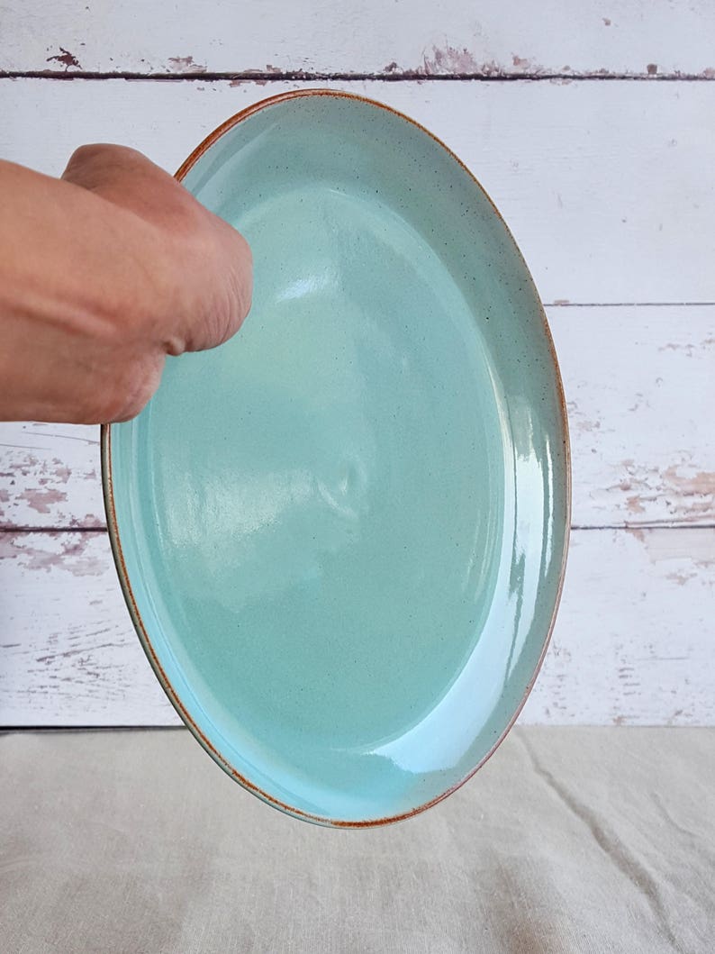 Może przedstawiać: Jasnoniebieski talerz ceramiczny z brązową obw&oacute;dką. Talerz jest okrągły i ma gładką, błyszczącą powierzchnię.