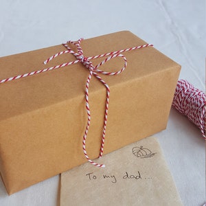 May include: A brown gift box tied with white and red twine. The box is sitting on a brown paper bag with the words "To my dad..." written on it.