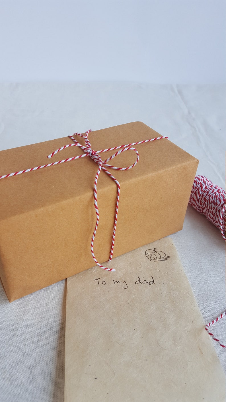 May include: A brown gift box tied with white and red twine. The box is sitting on a brown paper bag with the words "To my dad..." written on it.