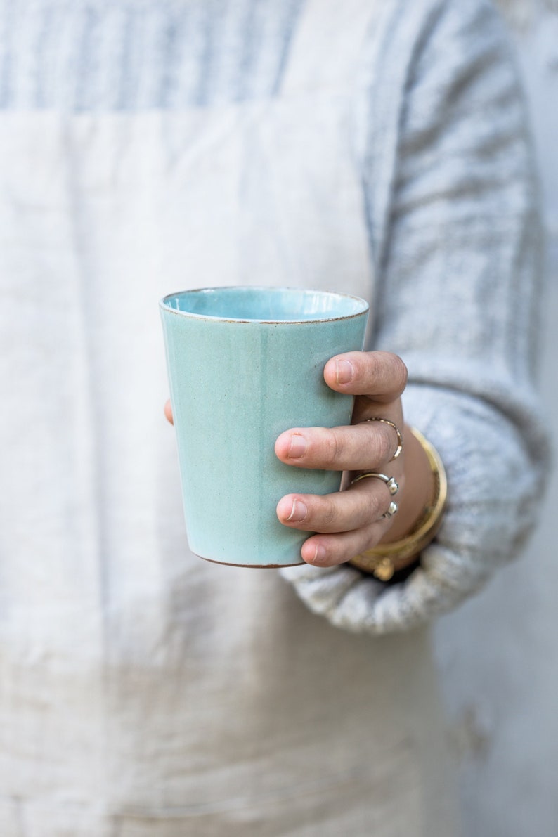 A handmade pottery Turquoise tumbler in a hand.
