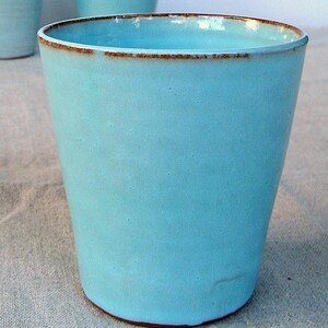 May include: A light blue ceramic mug with a brown rim. The mug is sitting on a light brown fabric surface.