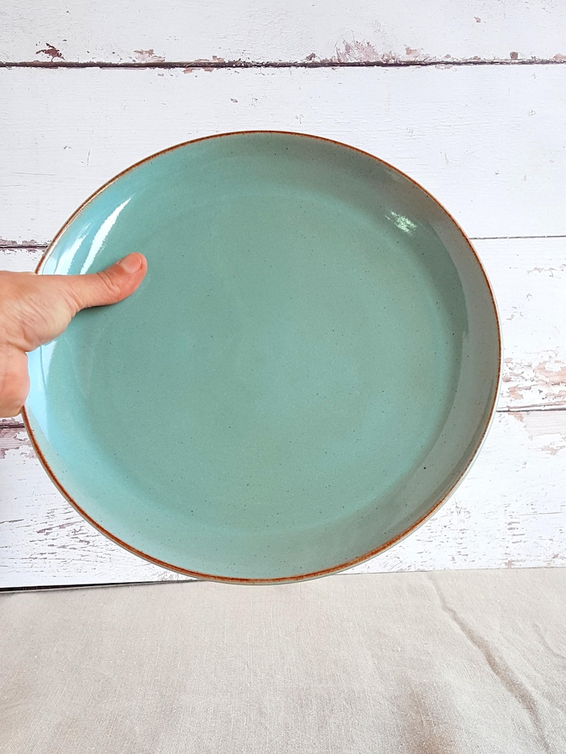 Może przedstawiać: Duży, okrągły, jasnoniebieski talerz ceramiczny z brązową obw&oacute;dką.