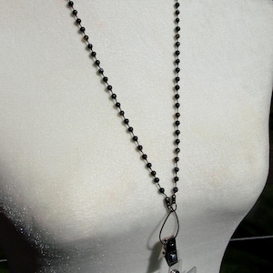 May include: A black beaded lanyard with a clear plastic ID holder. The lanyard is made of small, round beads and hangs around a mannequin's neck. The ID holder contains a photo. The lanyard is a practical accessory.