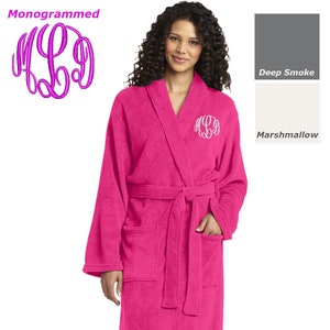 May include: A pink plush robe with a white monogrammed initial on the left chest. The robe has a matching belt and two pockets.