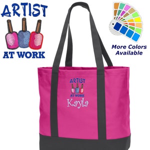 May include: Pink tote bag with black straps and a bottom. The bag has an embroidered design of three nail polish bottles with the text "Artist at Work Kayla".