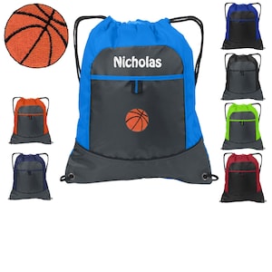 May include: A blue drawstring backpack with a gray pocket and a basketball design. The backpack has a zippered pocket and a drawstring closure. The backpack is personalized with the name "Nicholas".