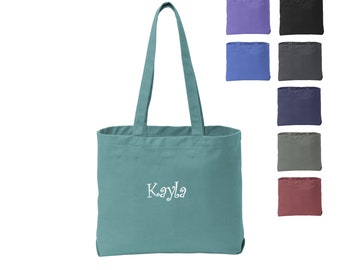 May include: A teal canvas tote bag with the name "Kayla" embroidered in white on the front. The bag has two long handles and is shown against a white background with a selection of other color options.