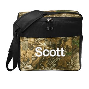 May include: A black and camouflage cooler bag with a shoulder strap and the name "Scott" printed on the front.