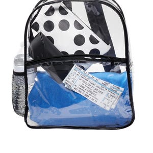 May include: Clear plastic backpack with black trim and zipper pulls. The backpack is filled with various items, including a black and white polka dot pouch, a blue blanket, a water bottle, and a concert ticket for Simon & Garfunkel. The ticket reads "WED NOV 5 2003 8:00 PM".