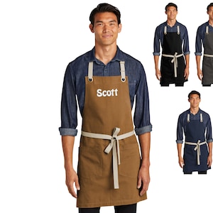 May include: A brown canvas apron with adjustable straps and a large pocket. The apron has a white embroidered name "Scott" on the front.