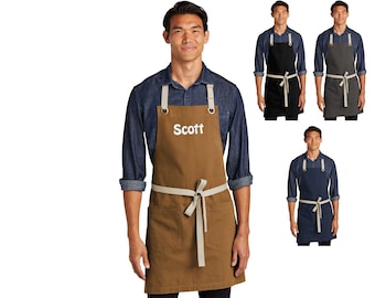 May include: A brown canvas apron with adjustable straps and a large pocket. The apron has a white embroidered name "Scott" on the front.