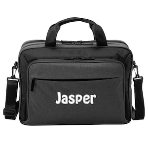 May include: A black and gray messenger bag with the name "Jasper" in white lettering on the front. The bag has a top handle, a shoulder strap, and a front zippered pocket. The bag is designed for carrying items.