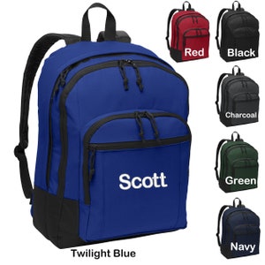 May include: A blue backpack with black accents and a zippered front pocket. The backpack has a black bottom and a white embroidered name "Scott" on the front. The backpack is shown against a white background with other color options displayed below.