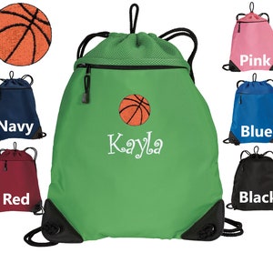 May include: Green drawstring bag with a black zipper and a black mesh panel. The bag has a white embroidered basketball and the name "Kayla". The bag is shown with other drawstring bags in different colors: pink, blue, red, and black.