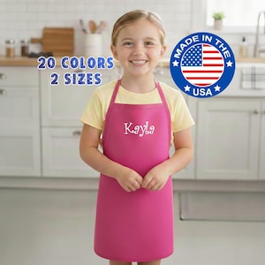 May include: A magenta apron with the name "Kayla" in white script. The apron is worn by a person wearing a yellow shirt. Text on the image reads "20 COLORS 2 SIZES" and a "Made in the USA" emblem.