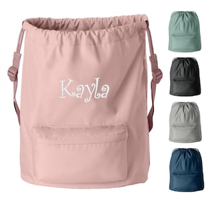 May include: A pink drawstring backpack with a front pocket and the name "Kayla" embroidered in white. The bag has adjustable straps and is shown with four other color options: green, black, gray, and navy blue.