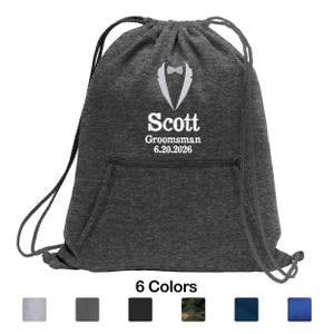 May include: A dark gray drawstring bag with a white tuxedo graphic and the name "Scott" printed below. The text "Groomsman 6.20.2026" is also printed on the bag. The bottom of the image shows six color options.
