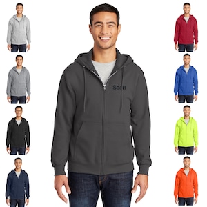 May include: A dark gray zip-up hoodie with a black embroidered logo that says "Scott". The hoodie has a hood with a drawstring and a front zipper. The model is wearing blue jeans.
