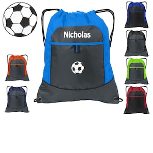 May include: A blue drawstring backpack with a gray pocket and a white soccer ball design. The backpack has a white embroidered name "Nicholas" on the front.