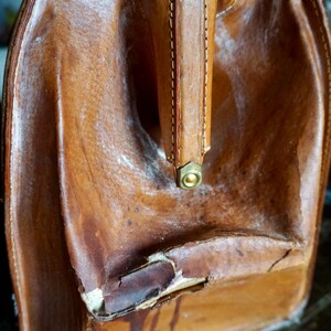 Puede incluir: Maleta de cuero marr&oacute;n vintage con asa y herrajes de lat&oacute;n. El equipaje usado muestra signos de edad, con desgaste visible en la superficie de cuero. El asa est&aacute; cosida y remachada.