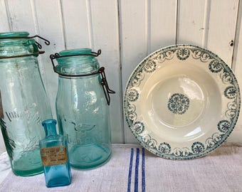 May include: An assortment of vintage glass jars and a decorative bowl. The jars are various sizes and shapes, with metal closures. The bowl is white with a blue floral pattern around the rim and center. The items are arranged on a white and blue striped cloth.