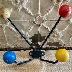 May include: A vintage-style wall hook with four colorful wooden knobs. The knobs are painted in red, yellow, blue, and green. The hook is made of black, twisted metal and has a black mounting plate. A decorative and functional item.