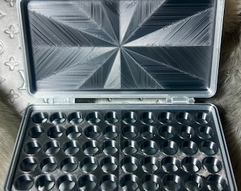 May include: A gray plastic storage case with a textured lid and a grid of 48 round compartments. The case is open and the compartments are empty.