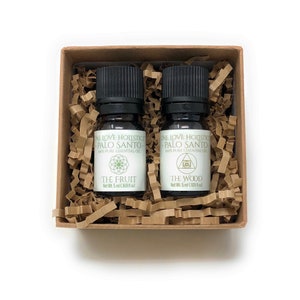 May include: Two small essential oil bottles in a brown box with shredded paper. The bottles have black caps and white labels with text that reads "ONE LOVE HOLISTICS PALO SANTO" and "THE FRUIT" and "THE WOOD". Each bottle contains 5 ml (0.169 fl oz) of oil.