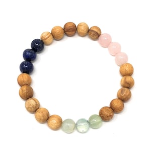 May include: A wooden beaded bracelet with blue, pink, and green gemstone beads. The bracelet is made of natural wood and features a variety of colours and textures.