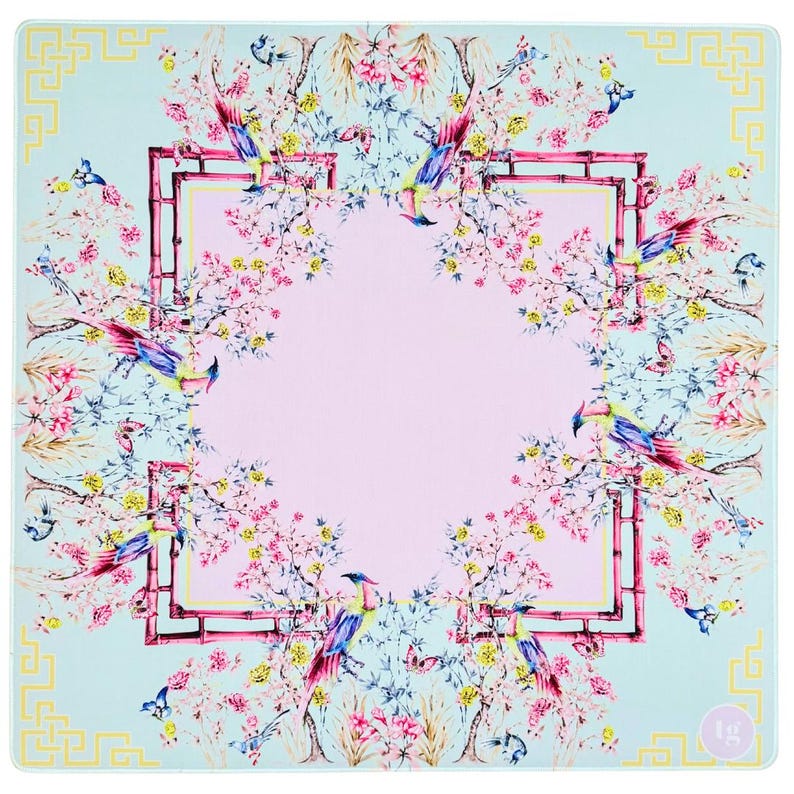 May include: Square, light blue decorative mat with a floral and bird design. The mat features a pink center, surrounded by a bamboo-style frame. Colorful birds and flowers are arranged around the frame. The corners have a yellow geometric pattern.