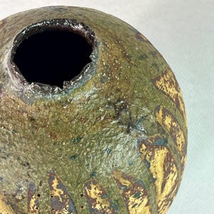 May include: A handcrafted ceramic vase with a textured surface. The vase features a dark opening and is primarily green and brown with yellow accents. The design includes vertical ridges and a speckled appearance, suggesting a rustic aesthetic.
