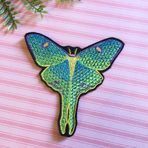 May include: A green and blue embroidered patch of a luna moth with a yellow body and purple accents.