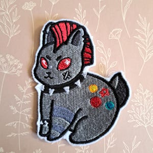 Pode incluir: Um remendo bordado cinza de um coelho punk rock com mohawk vermelho, colar de tachas pretas e pontos coloridos nas costas.