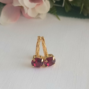 May include: A pair of gold hoop earrings with small, round, red gemstones.