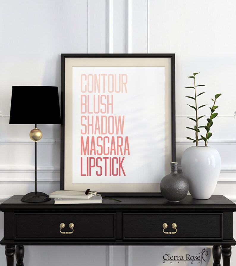 Puede incluir: Una impresi&oacute;n enmarcada en negro con las palabras "CONTOUR BLUSH SHADOW MASCARA LIPSTICK" en un degradado de rosa y rojo. La impresi&oacute;n est&aacute; sobre un fondo blanco y se encuentra sobre una mesa negra con dos cajones. Hay dos jarrones sobre la mesa, uno es blanco y el otro es gris.