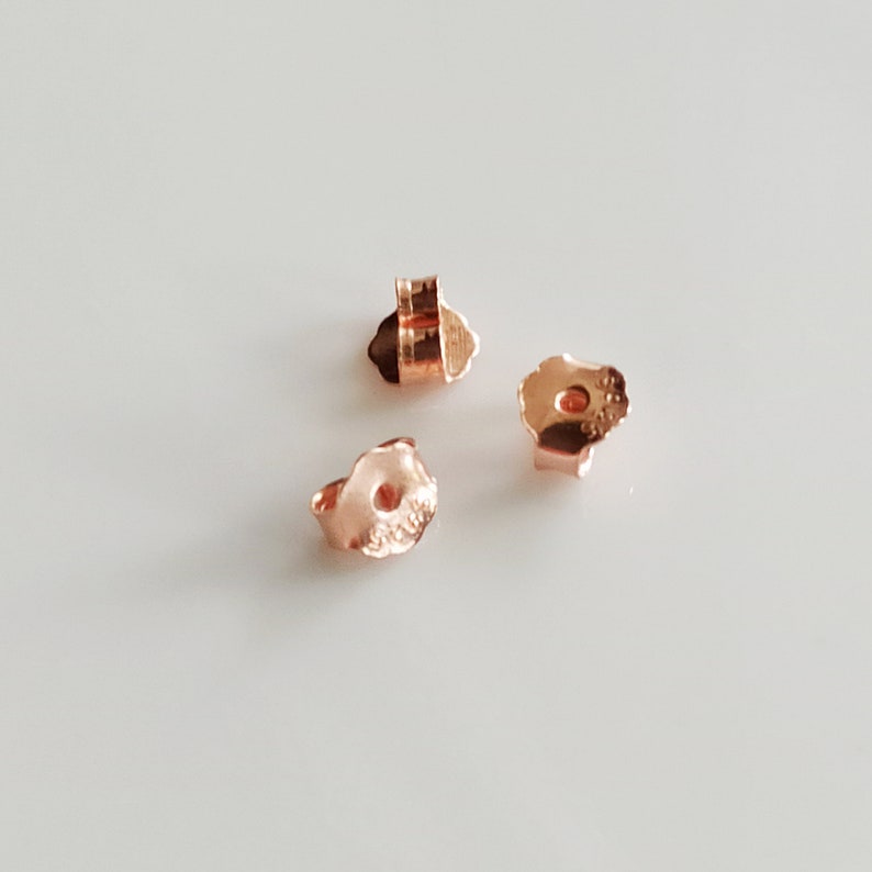 May include: Three gold-toned earring backs. The backs are shaped like a small flower with a hole in the centre.