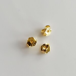 May include: Three gold-coloured earring backs. The backs are designed to secure earrings to the earlobe.