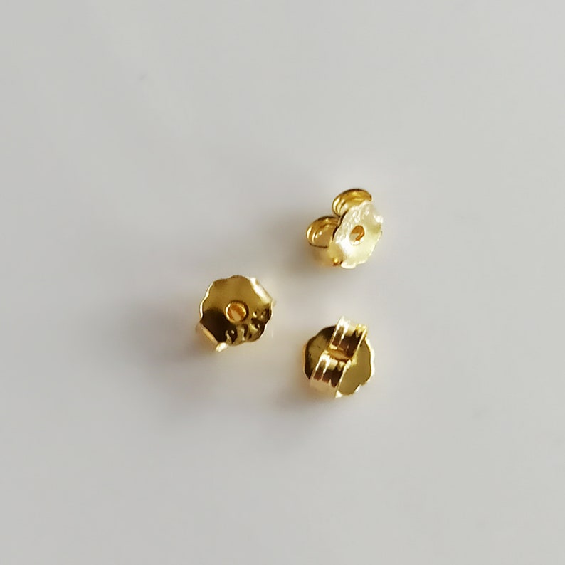 May include: Three gold-coloured earring backs. The backs are designed to secure earrings to the earlobe.