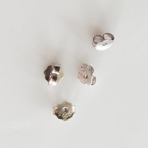 May include: Four silver earring backs, each with a small hole in the centre. The backs are designed to secure earrings to the earlobe.