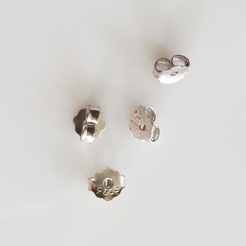 May include: Four silver earring backs, each with a small hole in the centre. The backs are designed to secure earrings to the earlobe.