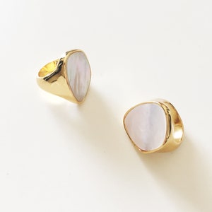 May include: Two gold rings with white pearlescent stones. The rings are in the shape of a teardrop.