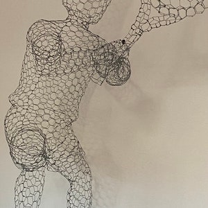 May include: A wire mesh sculpture of a person playing tennis. The sculpture is made of chicken wire and is painted in a metallic silver colour.