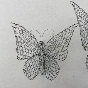 May include: A black wire butterfly sculpture with a hexagonal wire mesh design. The sculpture is made of thin wire and has a delicate, airy appearance.