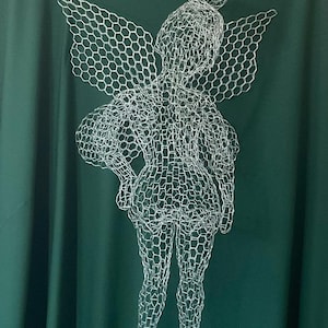 May include: A silver wire sculpture of a fairy with detailed wings, hair, and a dress. The fairy is set against a dark green backdrop. The sculpture is a unique piece of art, suitable for home decor.