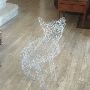 May include: A white wire mesh sculpture of a dog, standing on a light brown wood floor.