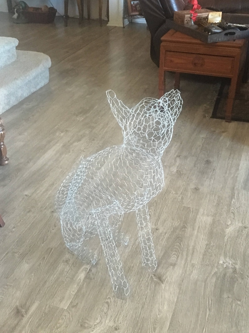 May include: A white wire mesh sculpture of a dog, standing on a light brown wood floor.