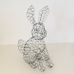 May include: A wire rabbit sculpture, made of a wire mesh, in a sitting position. The rabbit has long ears and a long tail.