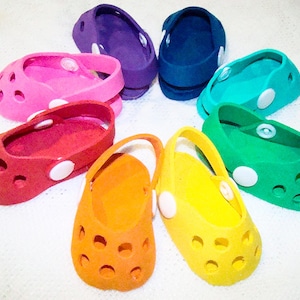 May include: A set of nine colorful miniature shoes with a rainbow color scheme. The shoes are made of a soft, flexible material and have a simple design with small holes.
