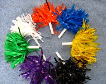 Könnte beinhalten: Ein Satz von acht bunten Plastik-Cheerleader-Pompons. Die Pompons sind in einem Kreis auf einer blauen Oberfläche angeordnet. Die Pompons sind weiß, orange, blau, gelb, grün, lila und schwarz.