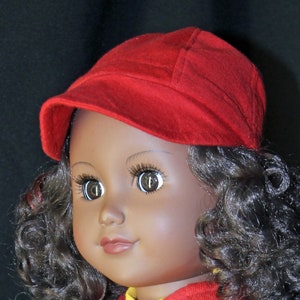 May include: A doll with brown skin and curly dark brown hair is wearing a red cap and a red and yellow shirt.